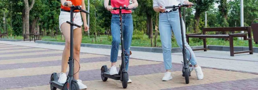 3 dziewczynki w parku jeżdżą na hulajnodze elektrycznej.