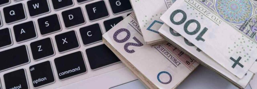 Banknoty 20PLN, 50PLN, 100 PLN leżące na klawiaturze laptopa. Logo Votum Odszkodowania