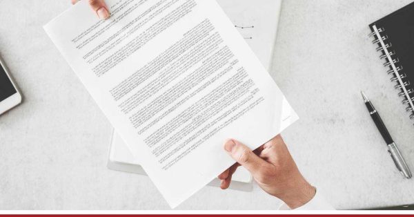 Osoby podają sobie dokument z rąk do rąk, w tle biurko