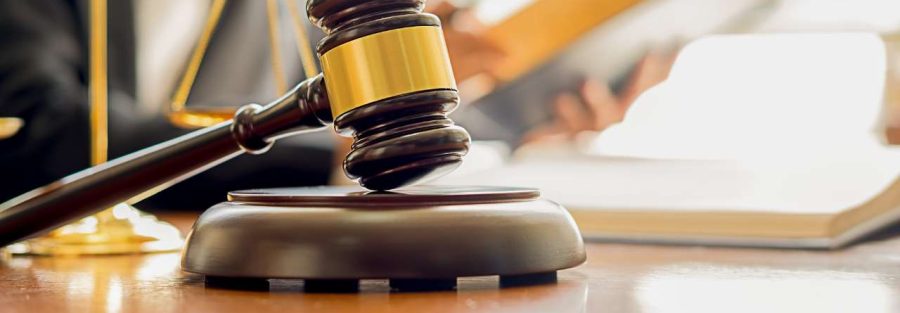 osoba czyta kodeks prawny, obok waga i młotek sędziowski