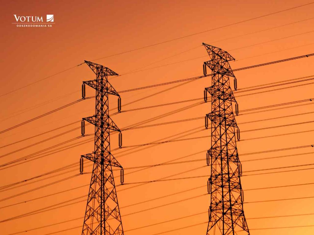 Słup energetyczny z liniami przesyłowymi i izolatorami na tle zachmurzonego nieba.