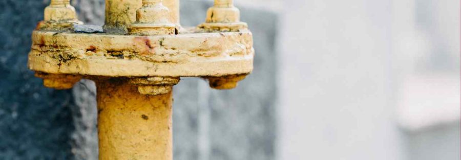 Zbliżenie na żółtą rurę gazową lub wodną z metalowym kołnierzem i śrubami, zamontowaną na tle szarej, kamiennej ściany.