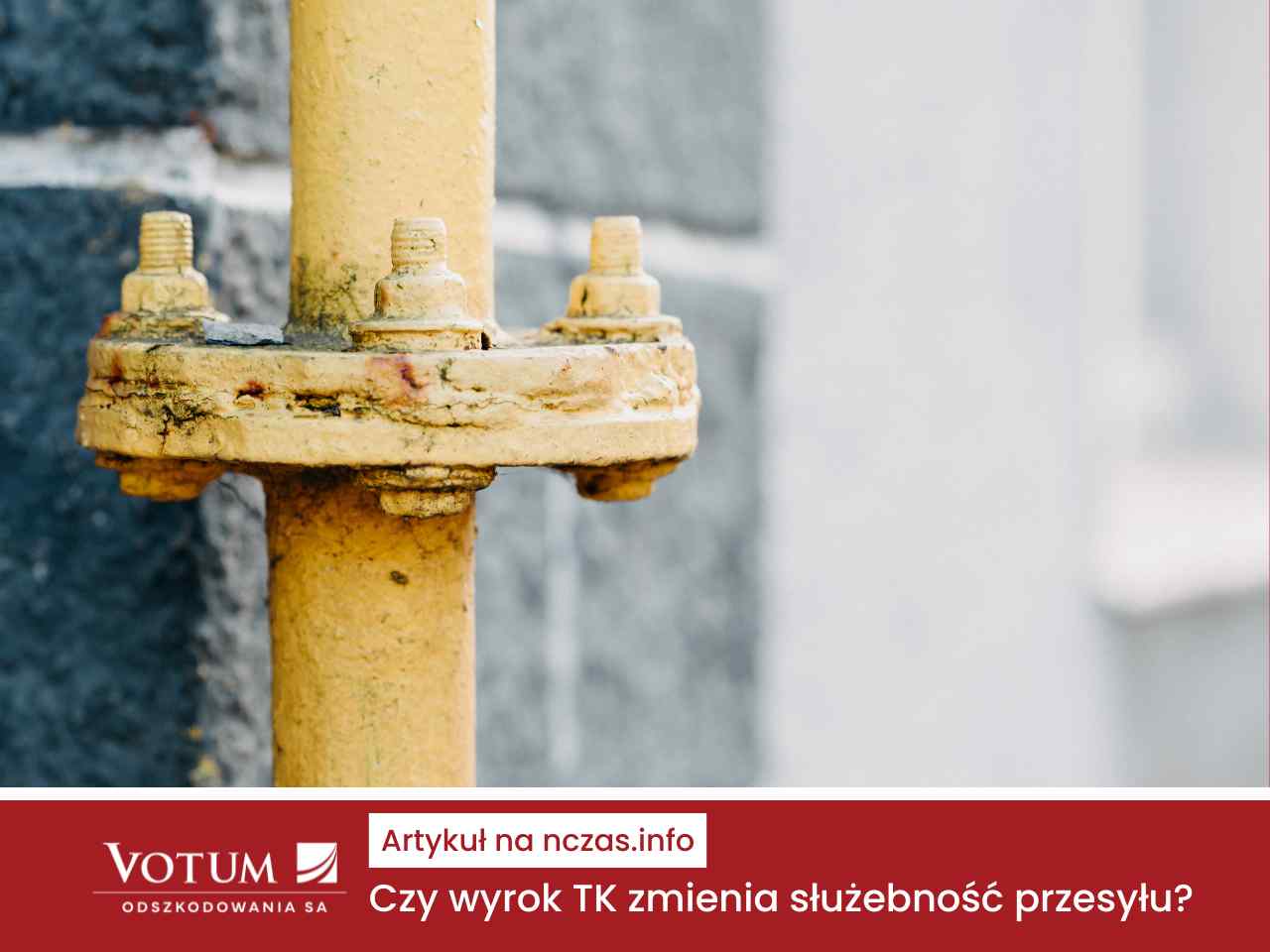 Zbliżenie na żółtą rurę gazową lub wodną z metalowym kołnierzem i śrubami, zamontowaną na tle szarej, kamiennej ściany.