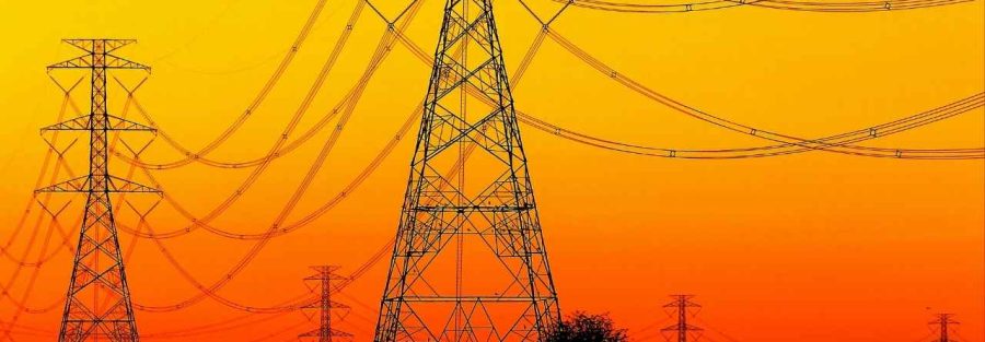 Wysokie słupy energetyczne na tle pomarańczowego zachodu słońca; grafika promocyjna z logo Votum Odszkodowania SA i tytułem artykułu o służebności przesyłu.