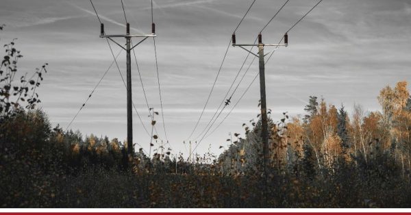 Słup energetyczny z liniami przesyłowymi i izolatorami na tle zachmurzonego nieba.