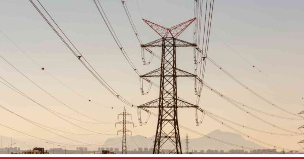 Słupy energetyczne z przewodami na tle nieba i pasma górskiego – baner z napisem Komentarz dla bankier.pl Votum Odszkodowania SA.