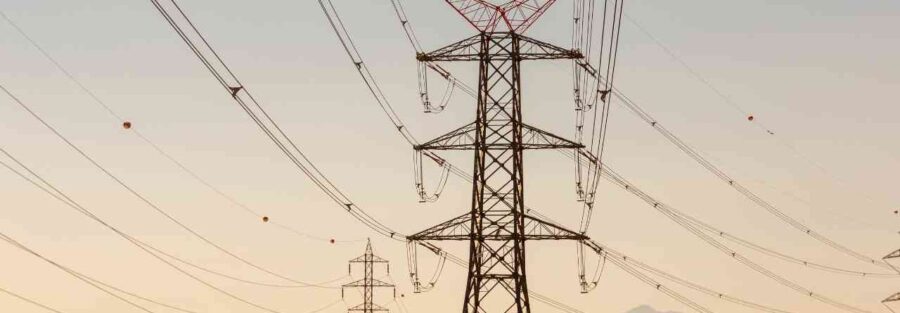 Słupy energetyczne z przewodami na tle nieba i pasma górskiego – baner z napisem Komentarz dla bankier.pl Votum Odszkodowania SA.