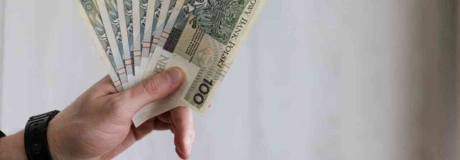 Męska dłoń trzyma wachlarz banknotów stuzłotowych na tle grafiki informacyjnej o rencie z OC sprawcy.